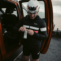 Person in cycling gear holding an All Real Cashew Cookie Dough Protein Bar next to an open car door.