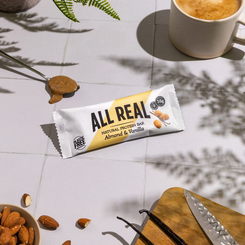 All Real almond vanilla protein bar with almonds, vanilla pods and coffee on table
