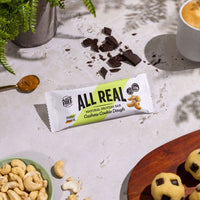 All Real cashew cookie dough protein bar with cashews and cookie dough bites on table