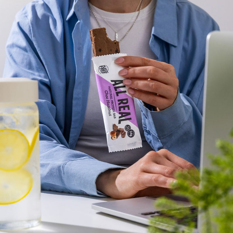 Person holding All Real chocolate hazelnut protein bar with bite