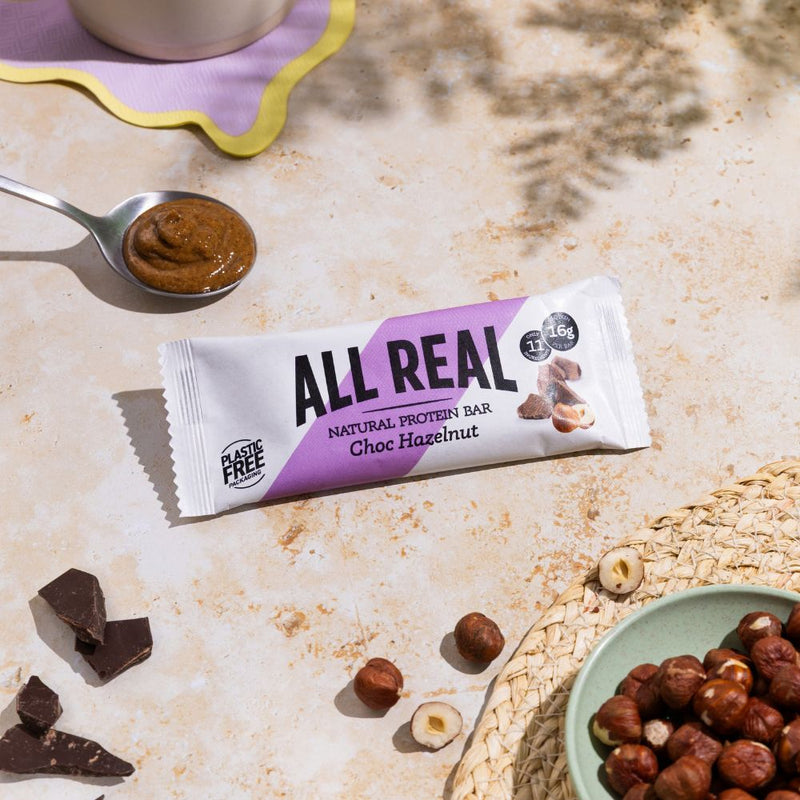 All Real chocolate hazelnut protein bar with hazelnuts and chocolate pieces on table