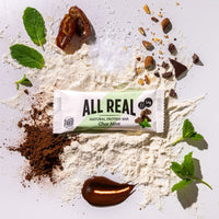 All Real chocolate mint protein bar with cocoa and fresh mint leaves on ingredient background