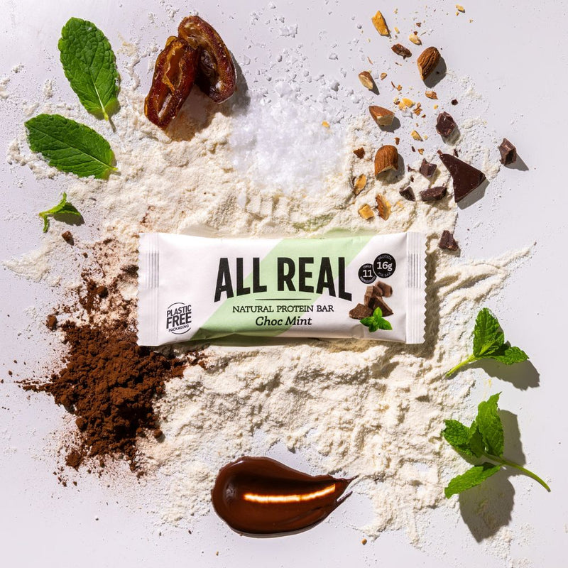 All Real chocolate mint protein bar with cocoa and fresh mint leaves on ingredient background