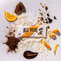 All Real chocolate orange protein bar with orange slices and cocoa ingredients scattered around