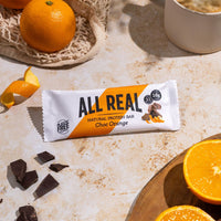 All Real chocolate orange protein bar with orange slices and chocolate pieces on table