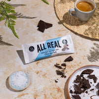 All Real chocolate sea salt protein bar with chocolate pieces and sea salt on table