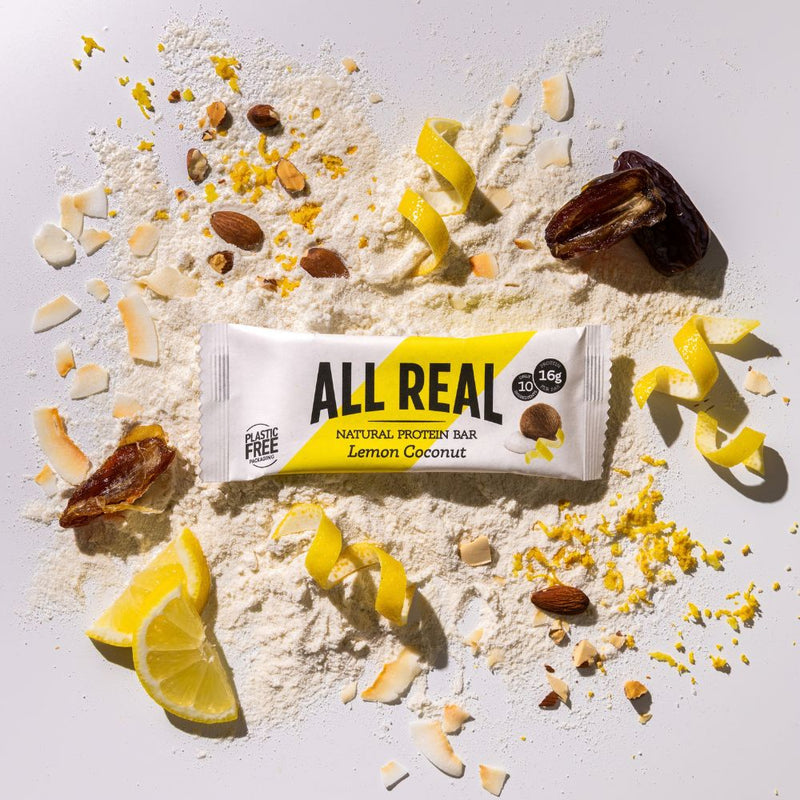 All Real lemon coconut protein bar with lemon slices and coconut ingredients scattered around
