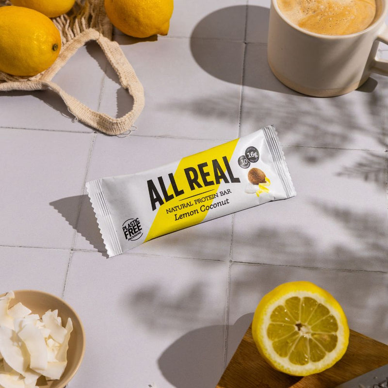 All Real lemon coconut protein bar on table with lemon slices, coffee and natural ingredients