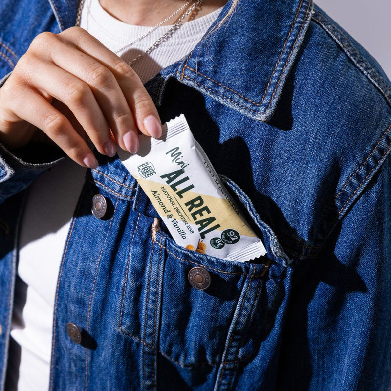 Person taking All Real mini almond protein bar from jacket pocket