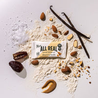 Mini All Real almond vanilla protein bar with almonds and vanilla pods on ingredient scatter