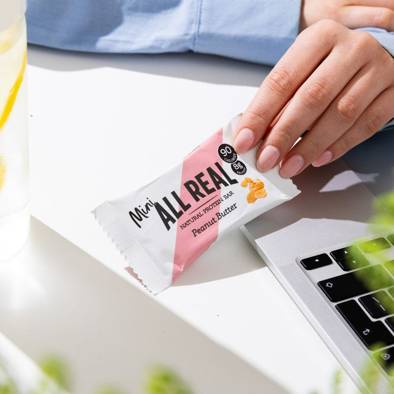 All Real mini peanut butter protein bar beside laptop on desk