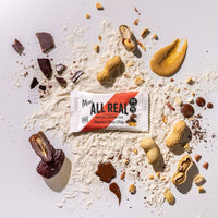 Mini All Real peanut chocolate chip protein bar with peanuts and chocolate chips on ingredient scatter