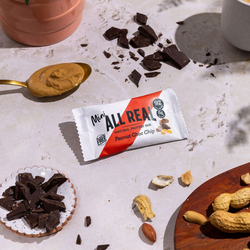 Mini All Real peanut chocolate chip protein bar with peanuts and chocolate pieces on table