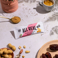 All Real peanut butter protein bar with peanuts and coffee in lifestyle setting