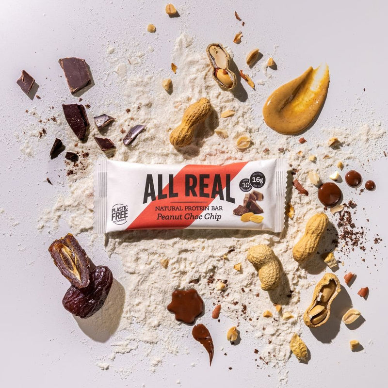 All Real peanut chocolate chip protein bar with peanuts and chocolate chips scattered around
