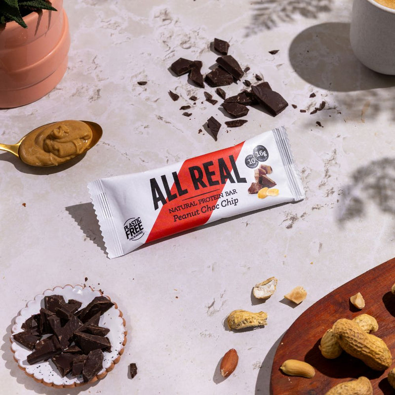All Real peanut chocolate chip protein bar with peanuts and chocolate pieces in lifestyle scene