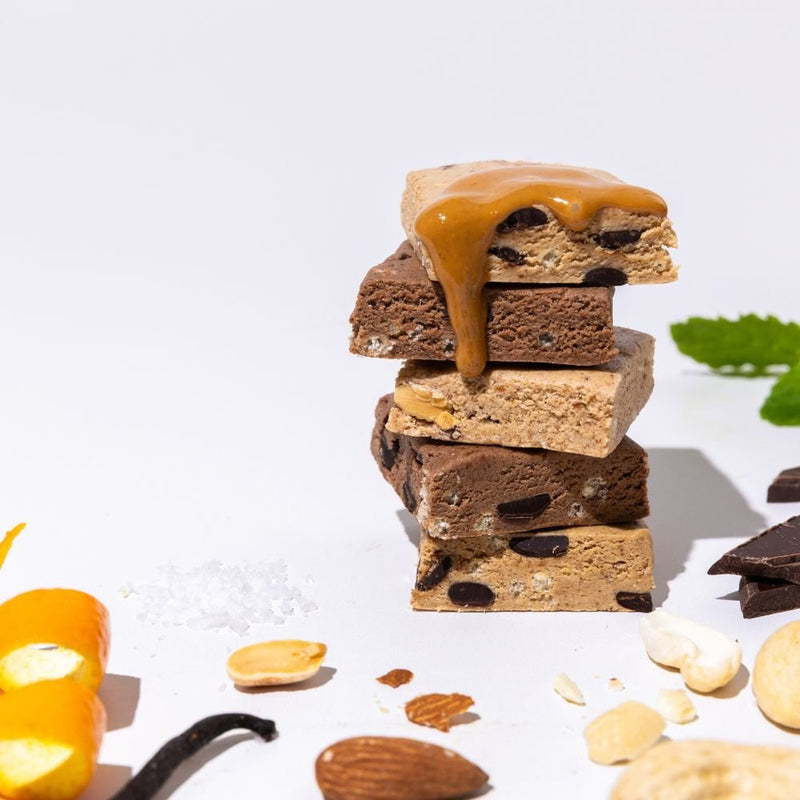 Stack of All Real protein bar pieces with chocolate drizzle and mixed ingredients on white background