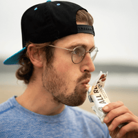 Man eating an All Real Almond Vanilla protein bar with a blurred background
