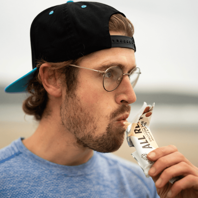 Man eating an All Real Almond Vanilla protein bar with a blurred background